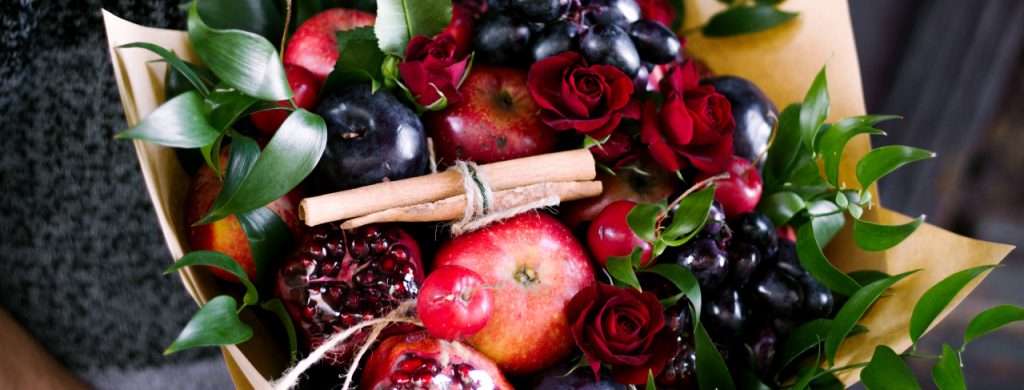 Arreglo floral con frutas frescas, incluyendo rosas rojas y manzanas, diseñado para celebraciones especiales y disponible en Bogotá.